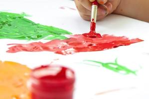 la main d'un enfant tient un pinceau et peint du papier à grands traits. frottis de peinture brillante sur papier blanc. photo