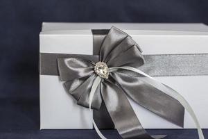 le coffret cadeau est blanc avec un joli noeud gris. cadeau sur fond sombre. vacances et surprises. nœuds en satin avec strass. photo