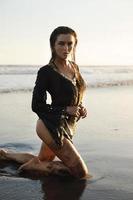 femme sexy portant une tunique noire pose sur la plage avec du sable noir