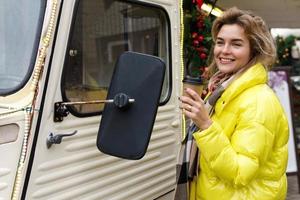 femme heureuse avec une tasse de café chaud à côté de la camionnette rétro au marché de noël photo