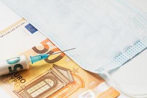 seringue en plastique remplie de papier-monnaie roulé, billet de cinquante euros et masque hygiénique jetable.