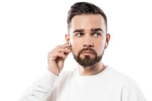 Bel homme barbu en vêtements blancs à l'aide d'écouteurs sans fil sur fond blanc photo