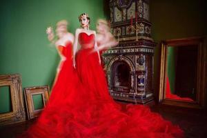 belle femme en robe longue rouge et en couronne royale près de la cheminée dans un intérieur de luxe en studio photo