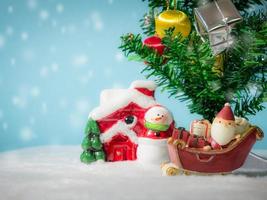 joyeux père noël avec une boîte de cadeaux sur le traîneau à neige allant à la maison. près de la maison ont bonhomme de neige et arbre de Noël. père noël et maison sur la neige. concept de noël et bonne année. photo
