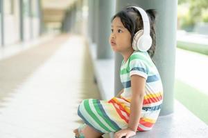 très jolie petite fille charmante et écoutant de la musique avec des écouteurs et était confortablement assise photo