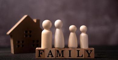 figures en bois famille debout sur un cube en bois qui écrit le mot famille devant une maison en bois. le concept de protection et de sécurité, de sécurité à domicile, d'assurance des biens et de maison. photo