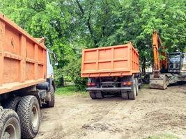 deux camions avec une carrosserie pour transporter des choses lourdes. autocollant robuste à l'arrière du corps. à côté se trouve une excavatrice orange pour creuser une tranchée photo