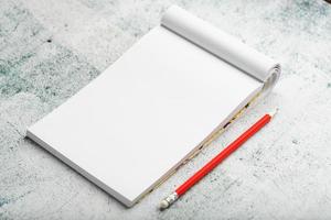 bloc-notes avec un crayon rouge sur fond de mur en plâtre blanc, pour l'éducation, écrire des objectifs et des actes photo