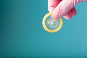 un préservatif ouvert dans une main dans un gant rose tient sur un fond bleu. latex pour la protection contre la grossesse. photo