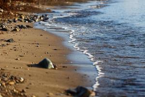 les vagues de la mer bleue avec de la mousse roulent sur le rivage doré. fermer photo