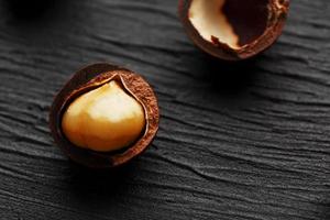 purifiée et la coquille répète les noix de macadamia sur fond de pierre texturée noire. concept d'alimentation saine photo