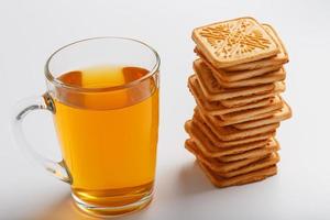 une pile de biscuits au blé doré et une tasse de thé vert parfumé sur fond blanc. biscuits disposés dans une colonne de petit-déjeuner et un point culminant doré avec des tasses à thé photo