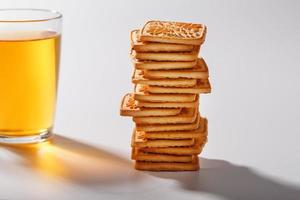 une pile de biscuits au blé doré et une tasse de thé vert parfumé sur fond gris. biscuits disposés dans une colonne de petit-déjeuner et un point culminant doré avec des tasses à thé photo