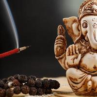 dieu hindou ganesh sur fond noir. statue de rudraksha et chapelet sur une table en bois avec un bâton d'encens rouge et de la fumée d'encens photo