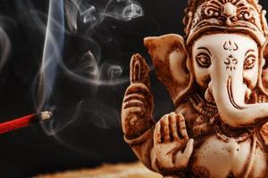 dieu hindou ganesh sur fond noir. statue de rudraksha et chapelet sur une table en bois avec un bâton d'encens rouge et de la fumée d'encens photo