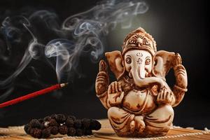 dieu hindou ganesh sur fond noir. statue de rudraksha et chapelet sur une table en bois avec un bâton d'encens rouge et de la fumée d'encens photo