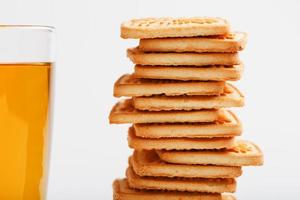 une pile de biscuits au blé doré et une tasse de thé vert parfumé sur fond blanc. biscuits disposés dans une colonne de petit-déjeuner et un point culminant doré avec des tasses à thé photo