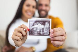 jeune femme enceinte et mari tenant une photo d'échographie et souriant.