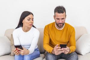 jeune femme jalouse avec smartphone regardant un petit ami souriant utilisant un smartphone à la maison, concept de problème relationnel. notion de méfiance