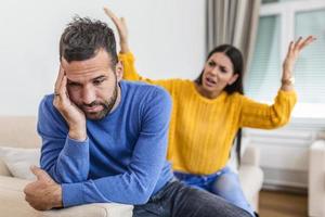 jeune couple se disputant - conflit, mauvaises relations. femme furieuse en colère. un jeune couple en colère s'assoit sur un canapé dans le salon en se disputant ou en se disputant en famille souffre d'un malentendu photo