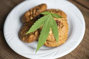 concept d'herbe de nature de nourriture de cannabis, biscuits au chocolat avec feuille de cannabis - plante de feuilles de marijuana sur fond sombre photo