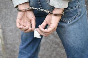 trafiquant de drogue arrêté dans les menottes de la police avec un petit paquet de drogue d'héroïne sur fond de mur sombre photo
