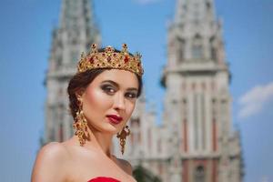 belle femme en robe longue rouge et en couronne royale près de la cathédrale catholique photo