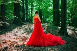 élégante femme élégante dans une longue robe rouge et une couronne royale dans la forêt brumeuse photo