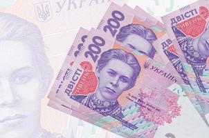 200 billets de hryvnias ukrainiens sont empilés sur fond de gros billets de banque semi-transparents. présentation abstraite de la monnaie nationale photo