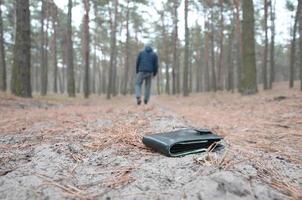 jeune homme perd son sac à main avec des billets en euros sur le chemin du bois de sapin d'automne russe. insouciance et perte de concept de portefeuille photo