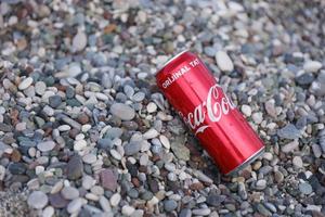 antalya, turquie - 18 mai 2022 la boîte de conserve rouge coca cola originale se trouve sur de petits cailloux ronds près du bord de mer. coca-cola sur la plage turque photo