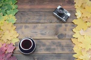 une tasse de thé et un vieil appareil photo parmi un ensemble de feuilles d'automne tombées jaunissantes sur une surface de fond de planches en bois naturel de couleur marron foncé