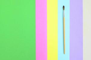 un nouveau pinceau se trouve sur un fond de texture de papier de couleurs pastel rose, bleu, vert, jaune, violet et beige dans un concept minimal. motif tendance abstrait photo