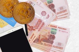 Billets de 5000 roubles russes et bitcoins dorés avec smartphone et cartes de crédit. concept d'investissement en crypto-monnaie. minage ou commerce de crypto photo