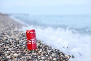 antalya, turquie - 18 mai 2022 la boîte de conserve rouge coca cola originale se trouve sur de petits cailloux ronds près du bord de mer. coca-cola sur la plage turque photo