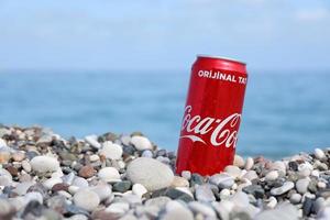antalya, turquie - 18 mai 2022 la boîte de conserve rouge coca cola originale se trouve sur de petits cailloux ronds près du bord de mer. coca-cola sur la plage turque photo