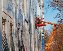 dnepropetrovsk, ukraine - 02.09.2022 constructeur dans un panier de grue répare le revêtement d'une structure métallique sur le mur de la façade d'un bâtiment. photo
