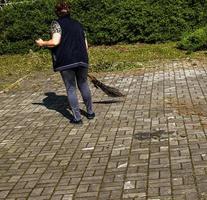 une femme balaie les feuilles mortes avec un balai dans la rue. le service municipal veille à la propreté de la ville. photo