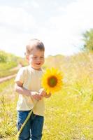 petit garçon mignon dans un champ de tournesols dans un t-shirt jaune se dresse et sourit.