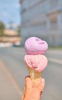 cornet de crème glacée à la main en gros plan avec bokeh. glace aux saveurs de fraise et de lavande. ambiance d'été. photographies de vacances. voyage en italie. idée de dessert avec espace de copie. photo