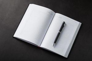 bureau avec un cahier ouvert noir et un stylo sur fond noir. photo