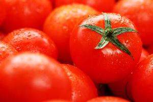 tomates rouges mûres, avec des gouttes de rosée. fond en gros plan avec texture de coeurs rouges avec des queues vertes. tomates cerises fraîches aux feuilles vertes. photo