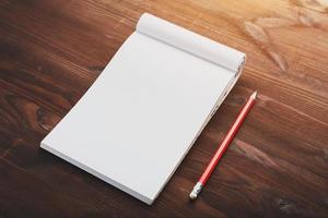 cahier avec un crayon rouge sur fond marron avec lumière du soleil chaude, pour l'écriture. espace vide libre pour écrire sur une feuille vierge d'un cahier. photo