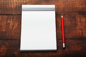 bloc-notes avec un crayon rouge sur fond de table en bois marron, pour l'éducation, écrire des objectifs et des actes photo