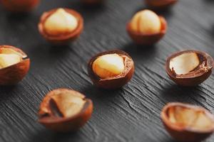 purifiée et la coquille répète les noix de macadamia sur fond de pierre texturée noire. concept d'alimentation saine. faible contraste photo