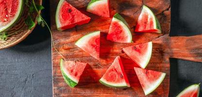 fruit frais de la pastèque coupé en morceaux sur une planche à découper en bois, le fruit de la pastèque a été coupé en deux, révélant sa chair rouge vif. photo