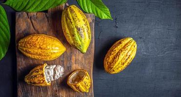 vue de dessus gousse de cacao jaune mûre fraîche et cacao en feuille verte sur fond noir photo