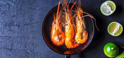 vue de dessus de crevettes de fruits de mer cuites dans une casserole ou de crevettes cuites et de citron vert sur fond noir photo