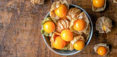 Vue de dessus des fruits mûrs de groseille du Cap jaune dans un bol d'acier inoxydable sur un fond de bois photo