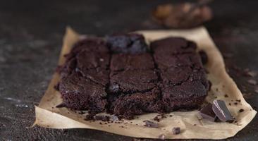 gâteaux de brownie spongieux au chocolat sur papier sulfurisé brun avec des morceaux de chocolat noir et de poudre de cacao, fond brun. photo